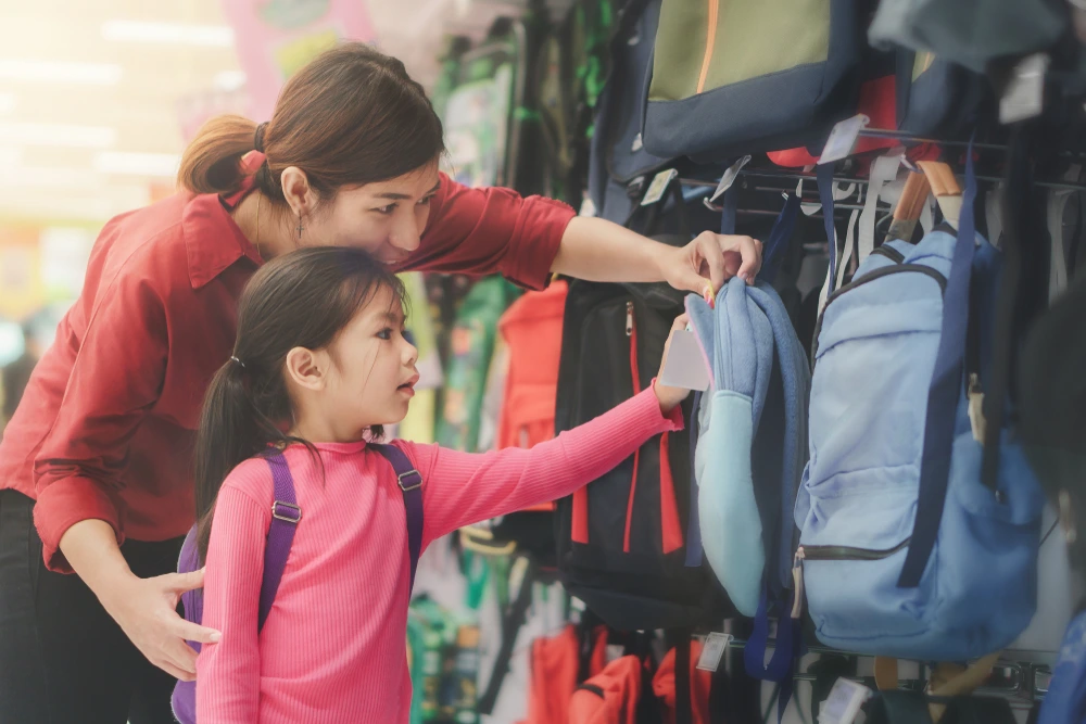 A mother helps her primary school age daughter shop for a backpack in a store