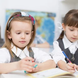 Two primary school girls sit at a desk writing in a workbook