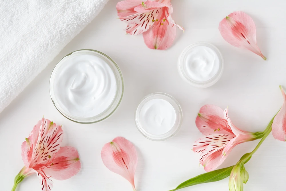 an overhead view of three jars filled with beauty cream on a white background. Orchids are placed around the jars as well