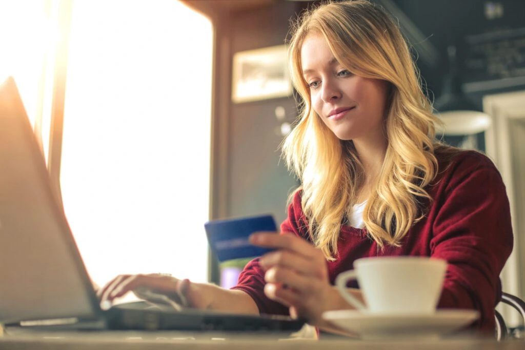 A blond woman sits at a laptop holding a credit card