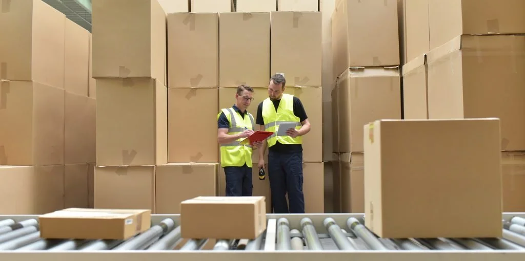 A photo of two men in a warehouse surrounded by cardboard boxes