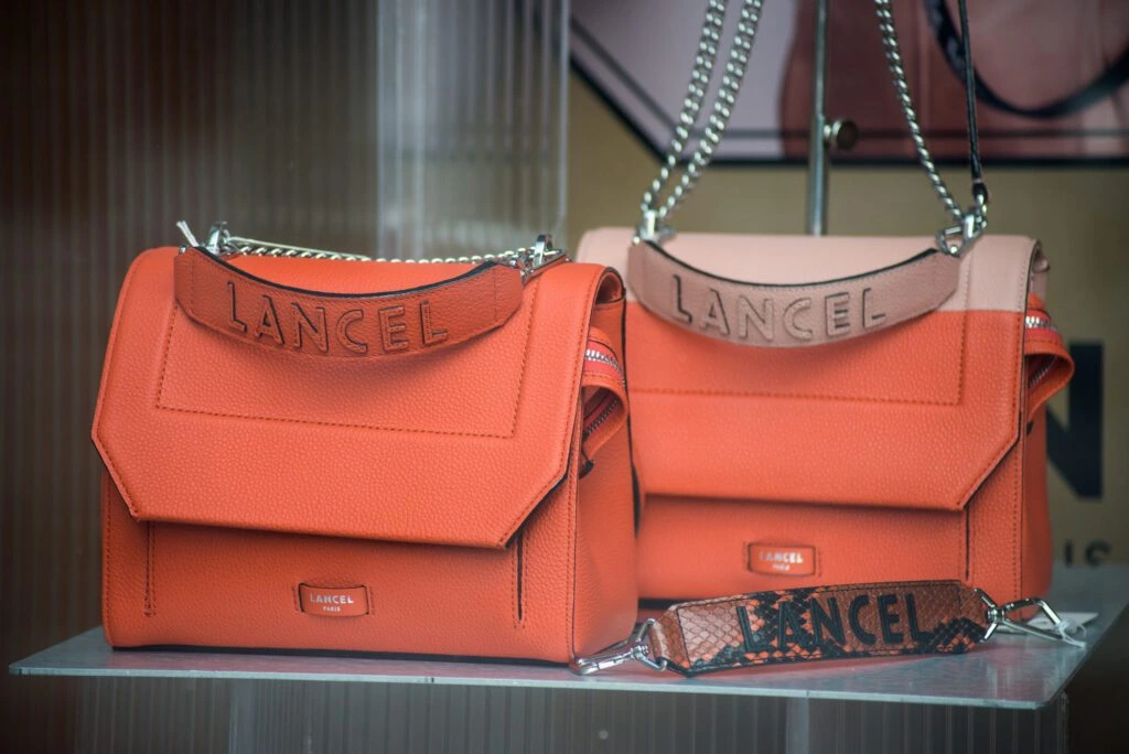 Two coral coloured luxury handbags are displayed on a glass shelf
