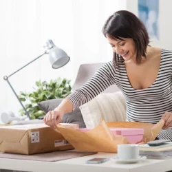 A woman in a black and white striped dress is opening a package. She is smiling.