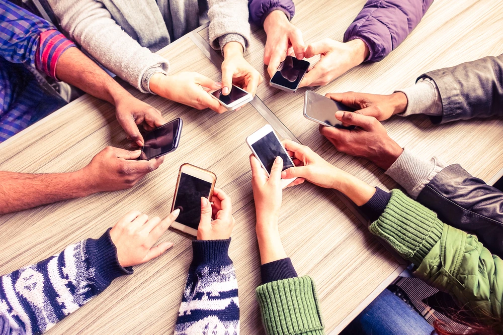 A photo of 6 people looking at their cell phones. top view and only their arms are visible