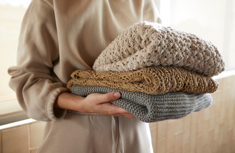A woman hold three folded, earth-tone cotton sweaters illustrating the finished product in the supply chain