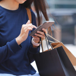 A close up of a woman on her phone holding shopping bags