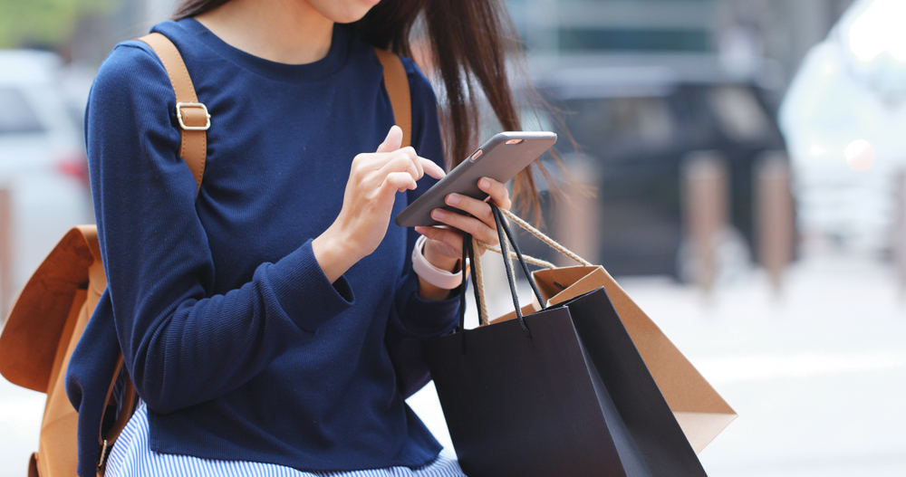 A close up of a woman on her phone holding shopping bags