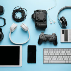 Consumer electronics including headphones, a tablet, a smartphone, video game controller and keyboard are arranged in rows on a light blue background