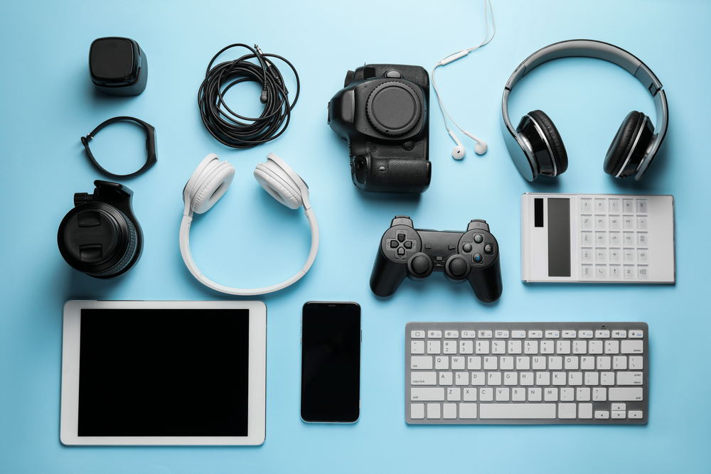 Consumer electronics including headphones, a tablet, a smartphone, video game controller and keyboard are arranged in rows on a light blue background