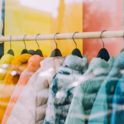 yellow, orange, pink, green and blue puffer jackets hang in a store window