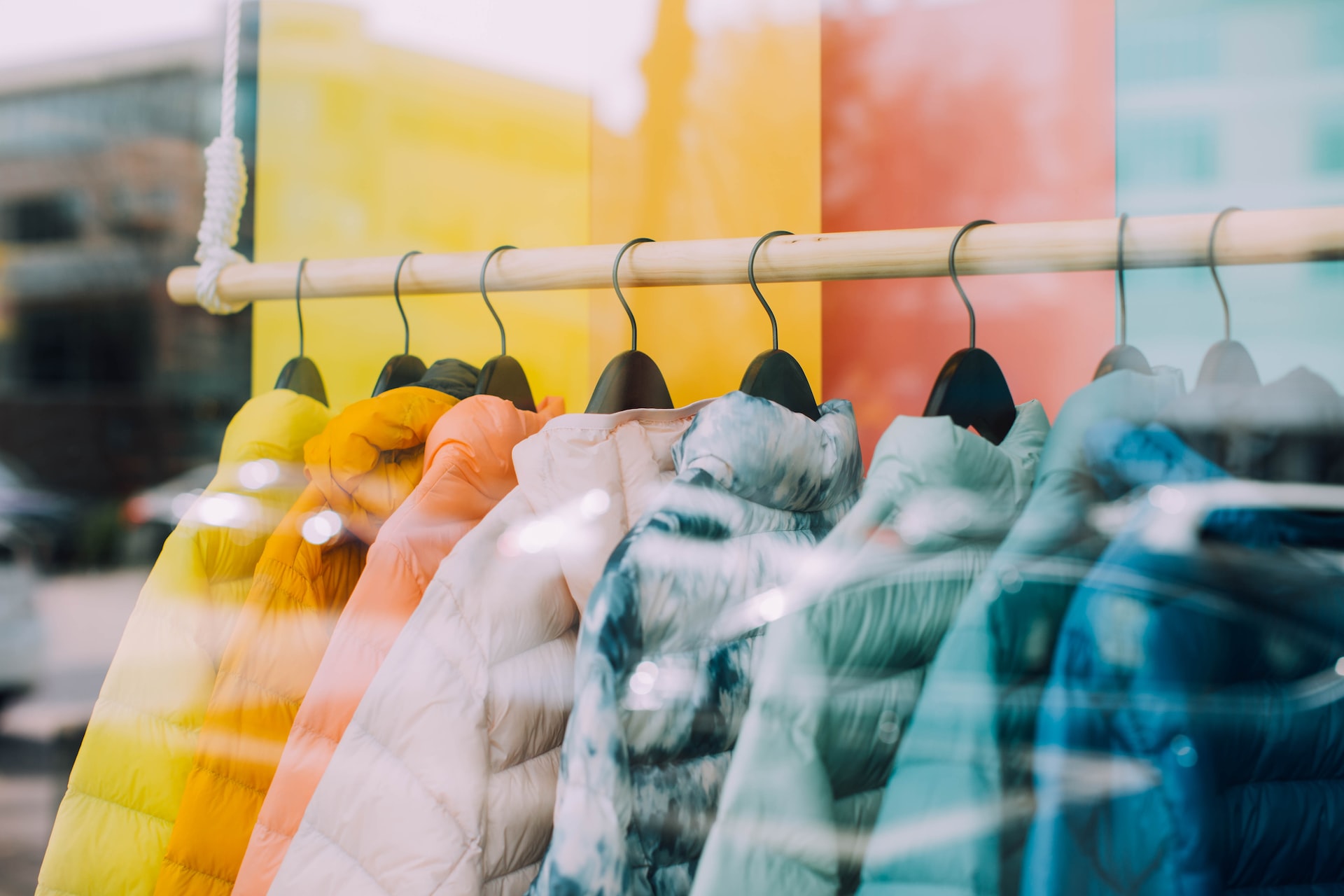 yellow, orange, pink, green and blue puffer jackets hang in a store window