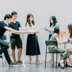 A group of young shoppers stand and sit around tables using laptops and talking to each other