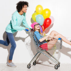 a young man pushes a young woman holding balloons in a shopping cart